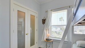 A bedroom with a bed, a window with blinds, a bedside table with a lamp, and a wardrobe. - Group-Friendly Hot Tub Haven in Galveston! (Galveston)