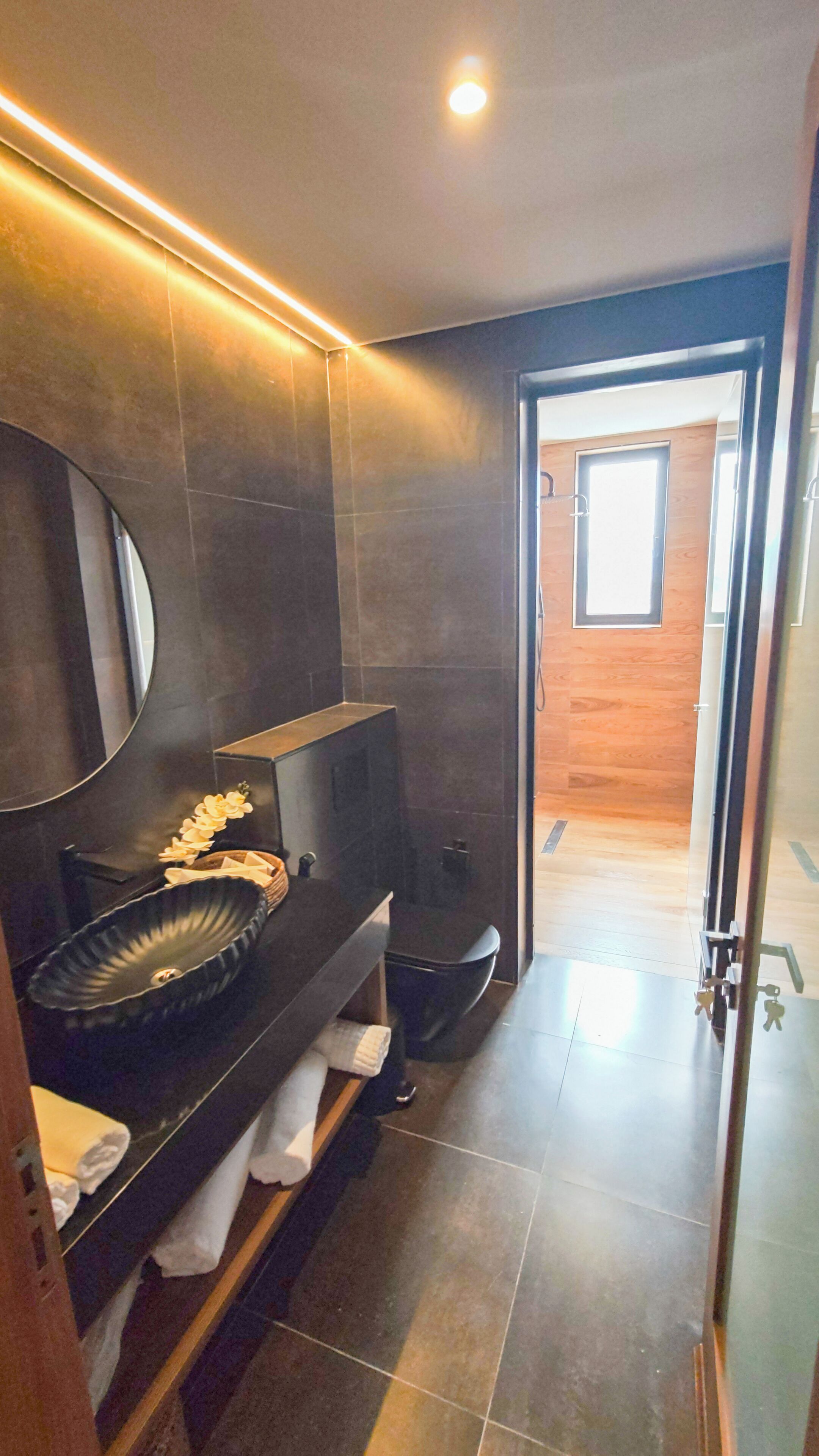 A modern bathroom with a large mirror, a black sink, and a shower area.
