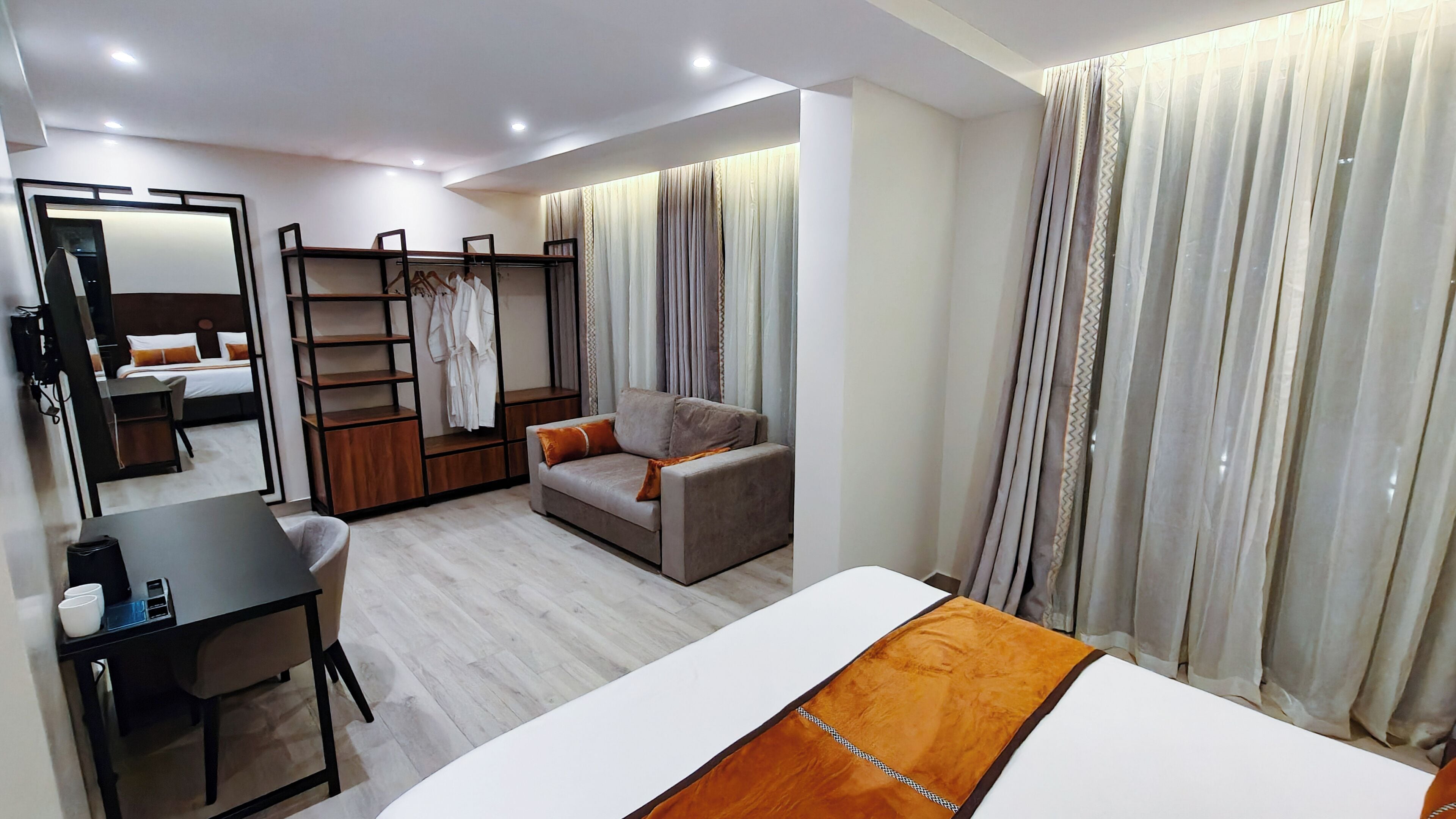 Una habitación de hotel moderna con cama, sofá, escritorio, silla, armario y espejo.