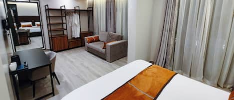 Una habitación de hotel moderna con cama, sofá, escritorio, silla, armario y espejo.
