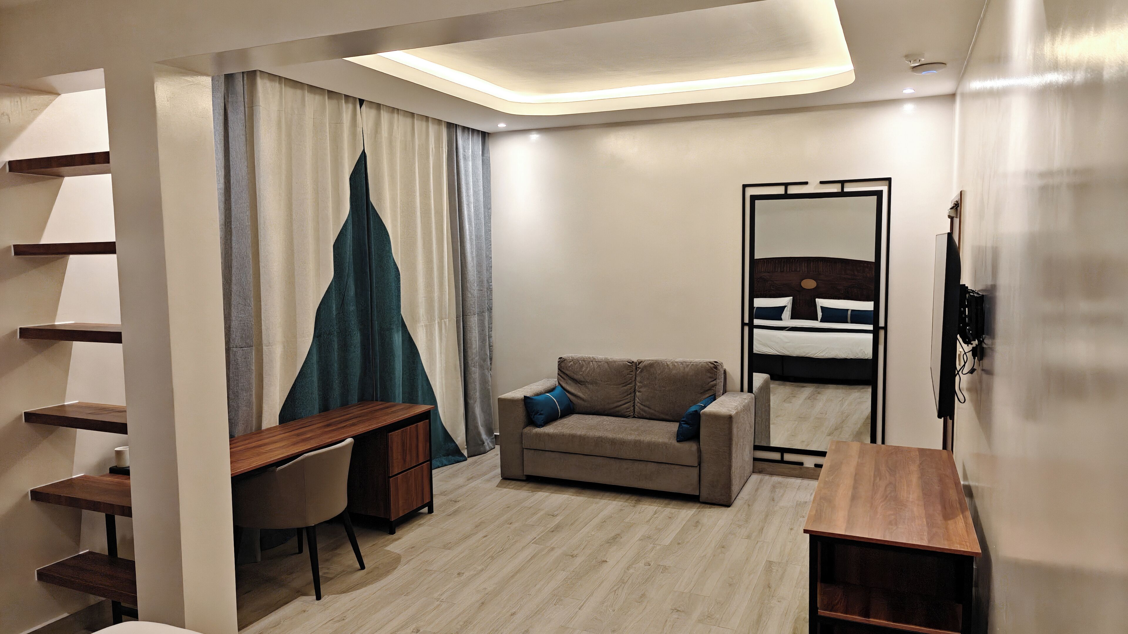 A modern hotel room with a desk, sofa, and a bed with a headboard.