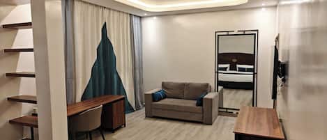 A modern hotel room with a desk, sofa, and a bed with a headboard.