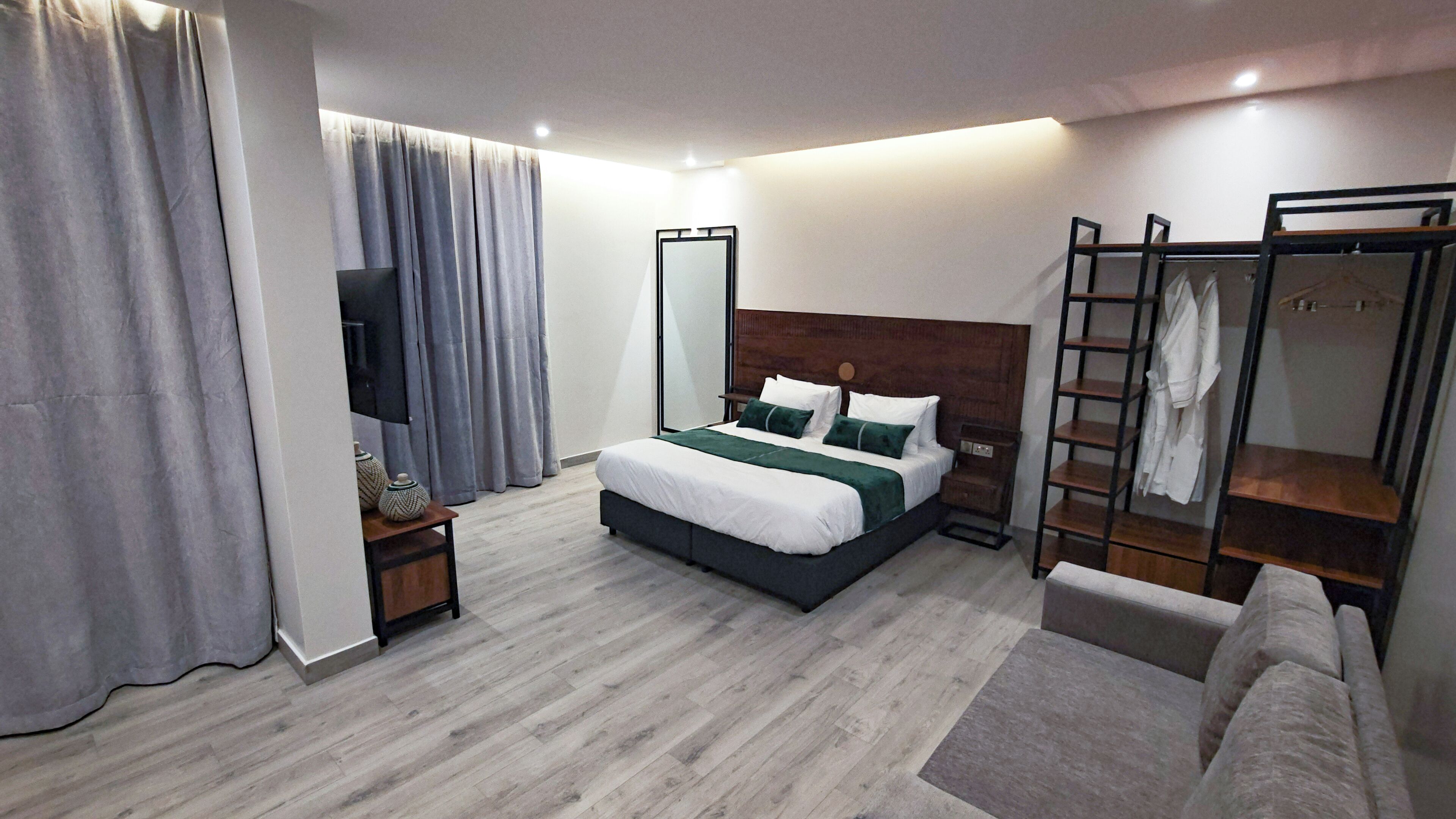 Una habitación de hotel moderna con una cama grande, televisión, armario y zona de estar.