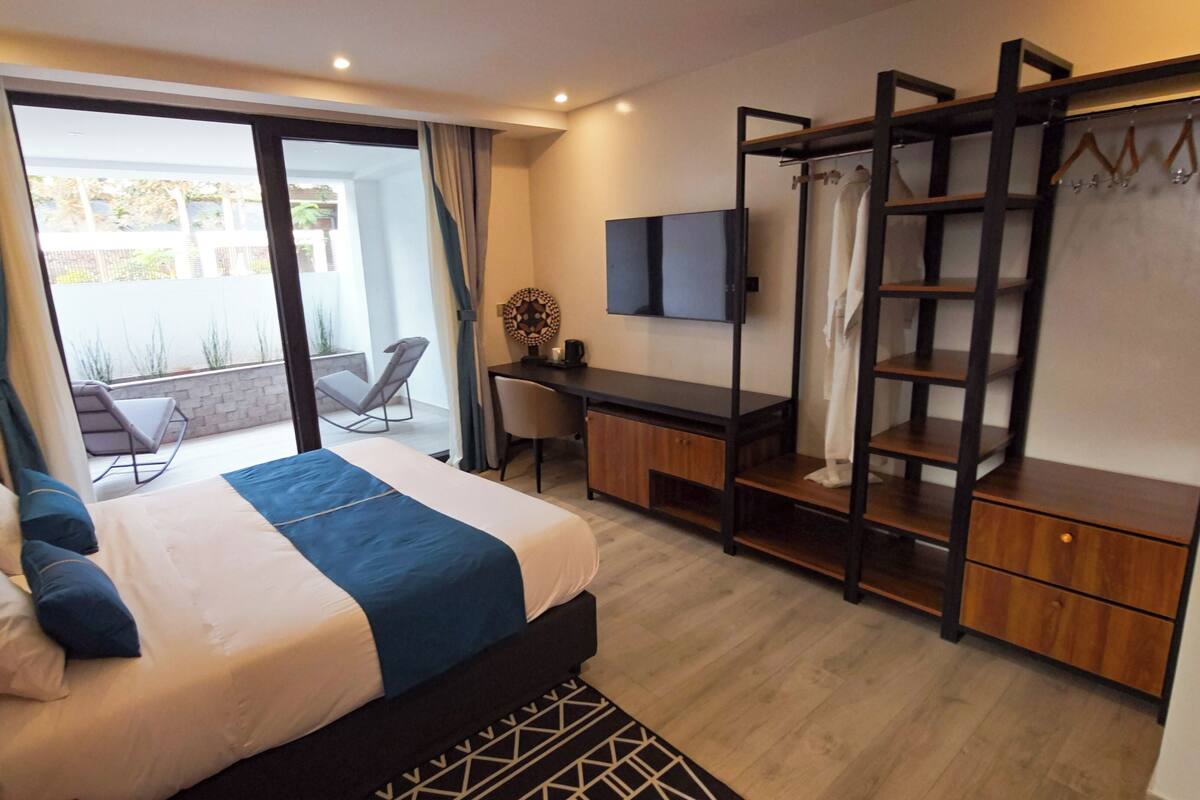 A hotel room with a bed, a desk, a chair, a TV, and a balcony with a view.