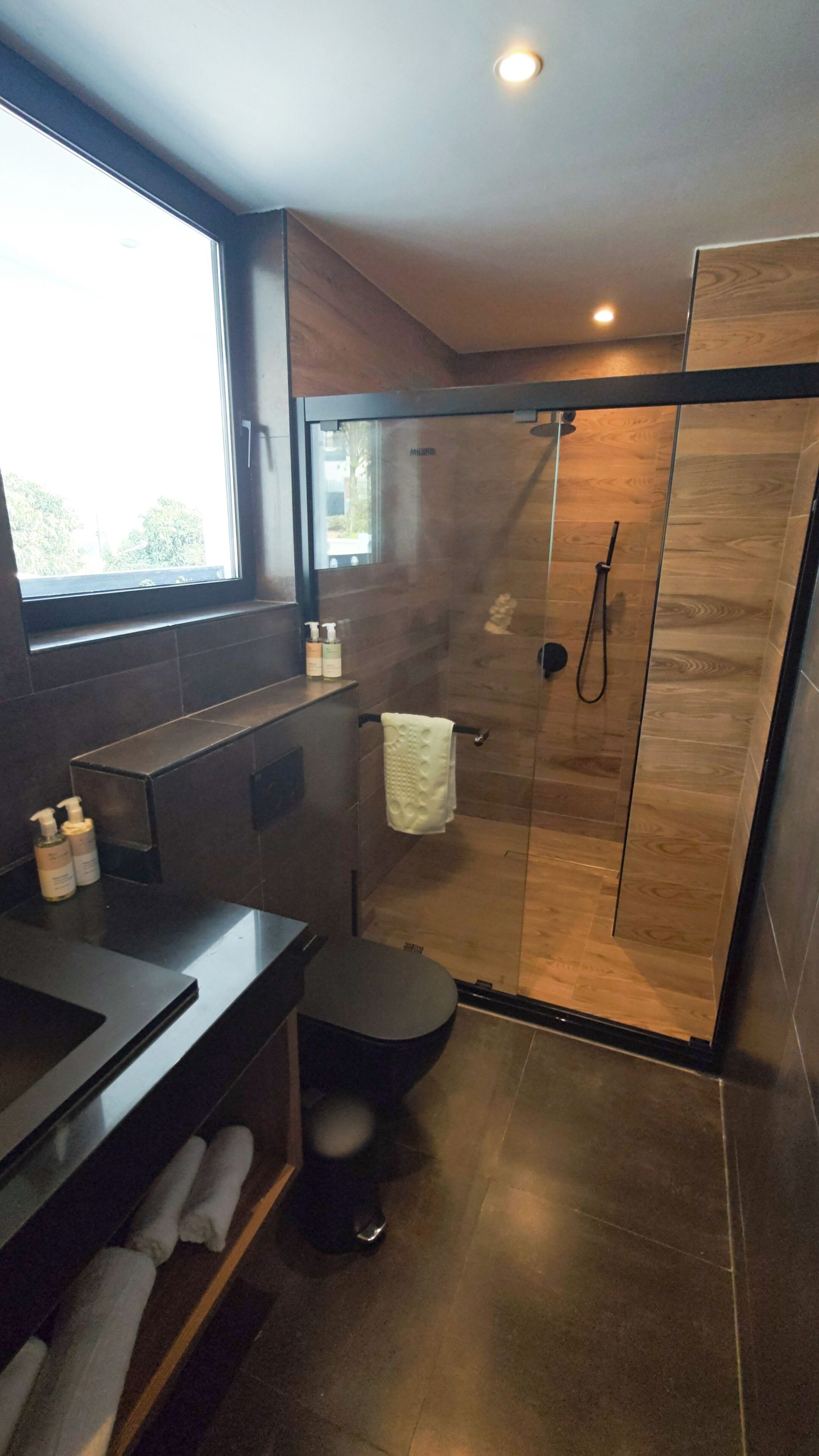 Un baño moderno con cabina de ducha de vidrio, tocador con espejo y ventana que proporciona luz natural.