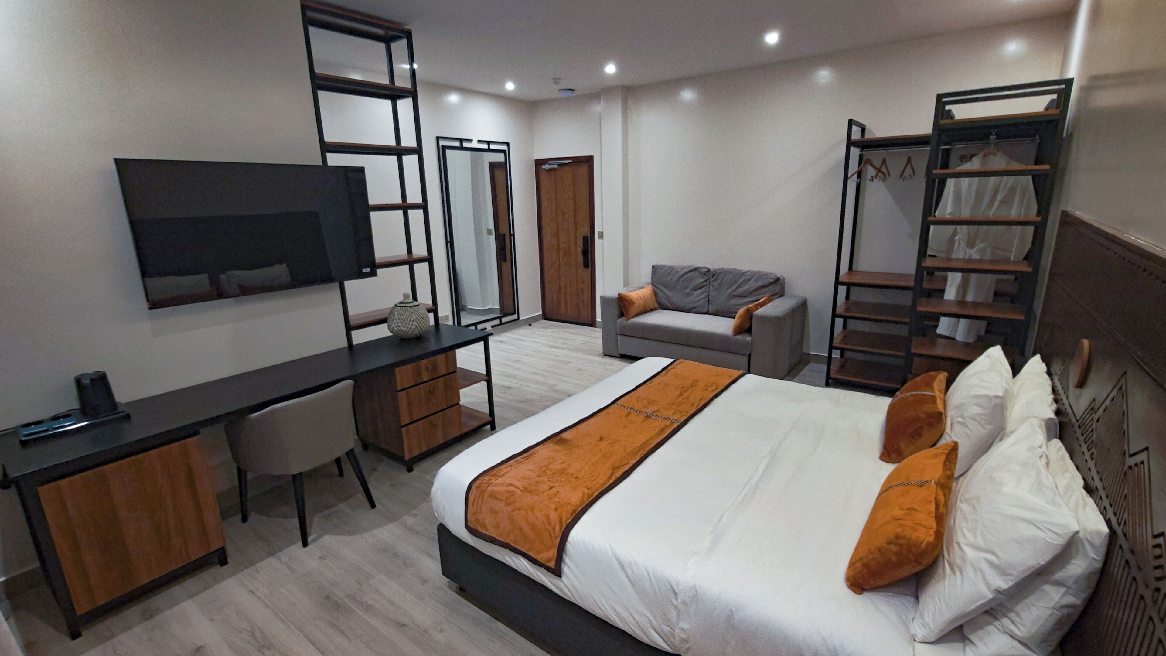 Una habitación de hotel moderna con cama, escritorio, silla, televisor, armario y zapatero.