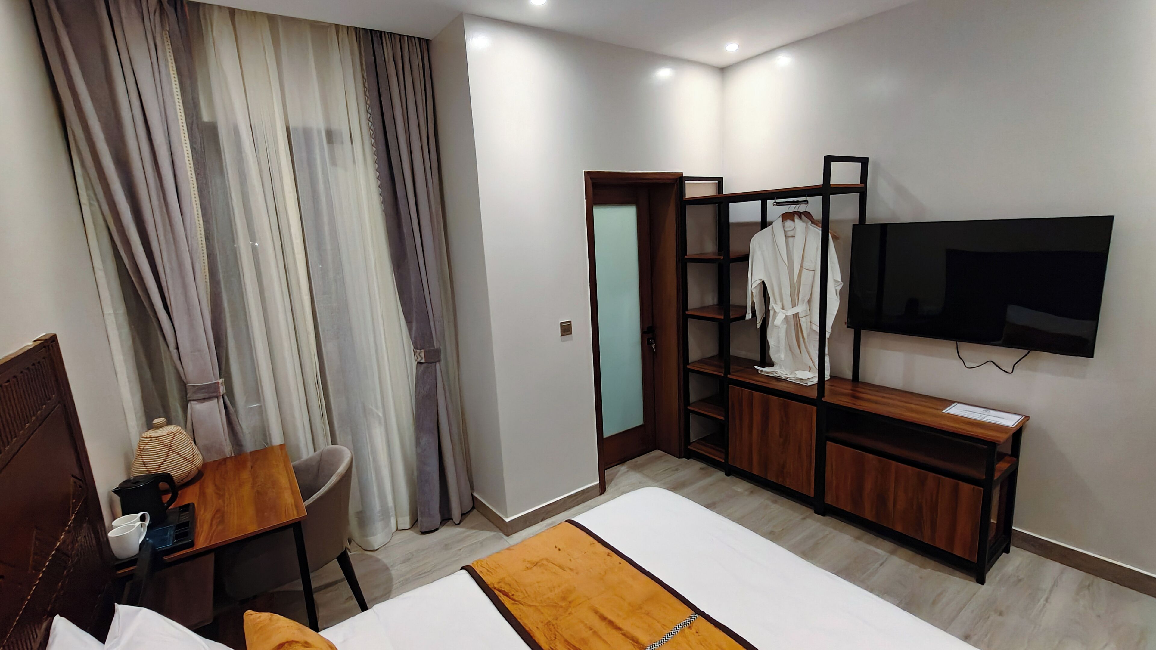 A hotel room with a bed, a desk with a chair, a TV mounted on the wall, and a wardrobe with shelves.