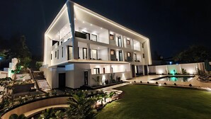 Un hotel moderno de varios pisos con piscina, iluminación exterior y un jardín bien cuidado.