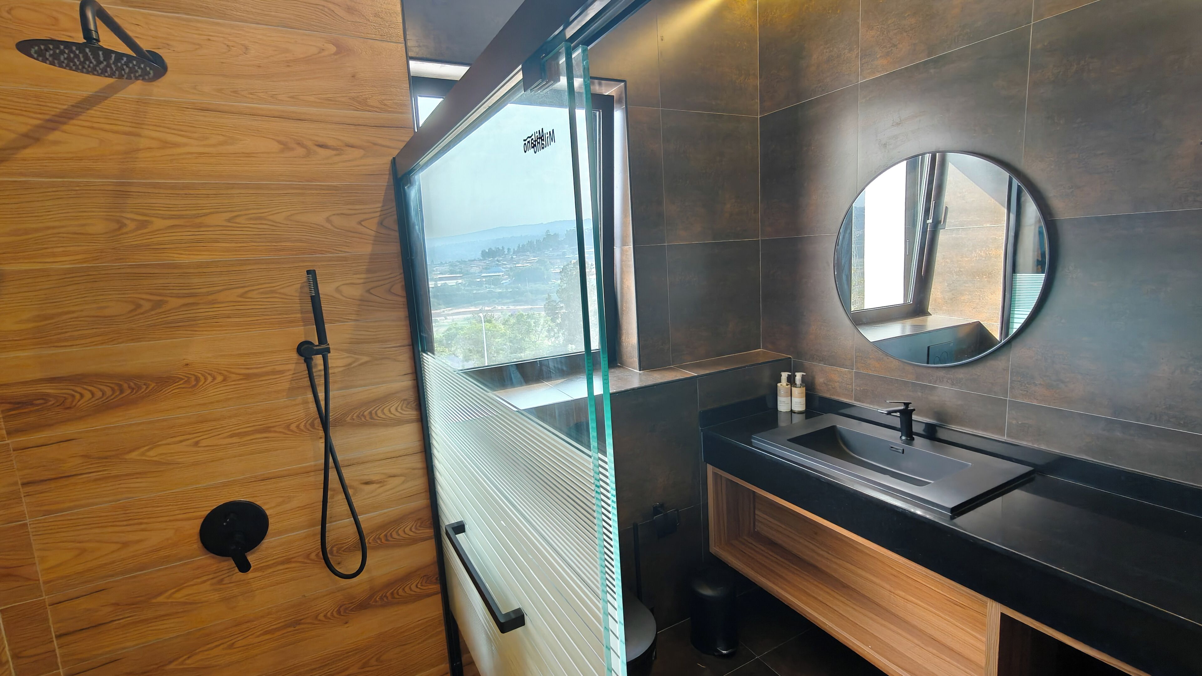 A modern bathroom with a wooden vanity, a round mirror, and a shower with a glass door.