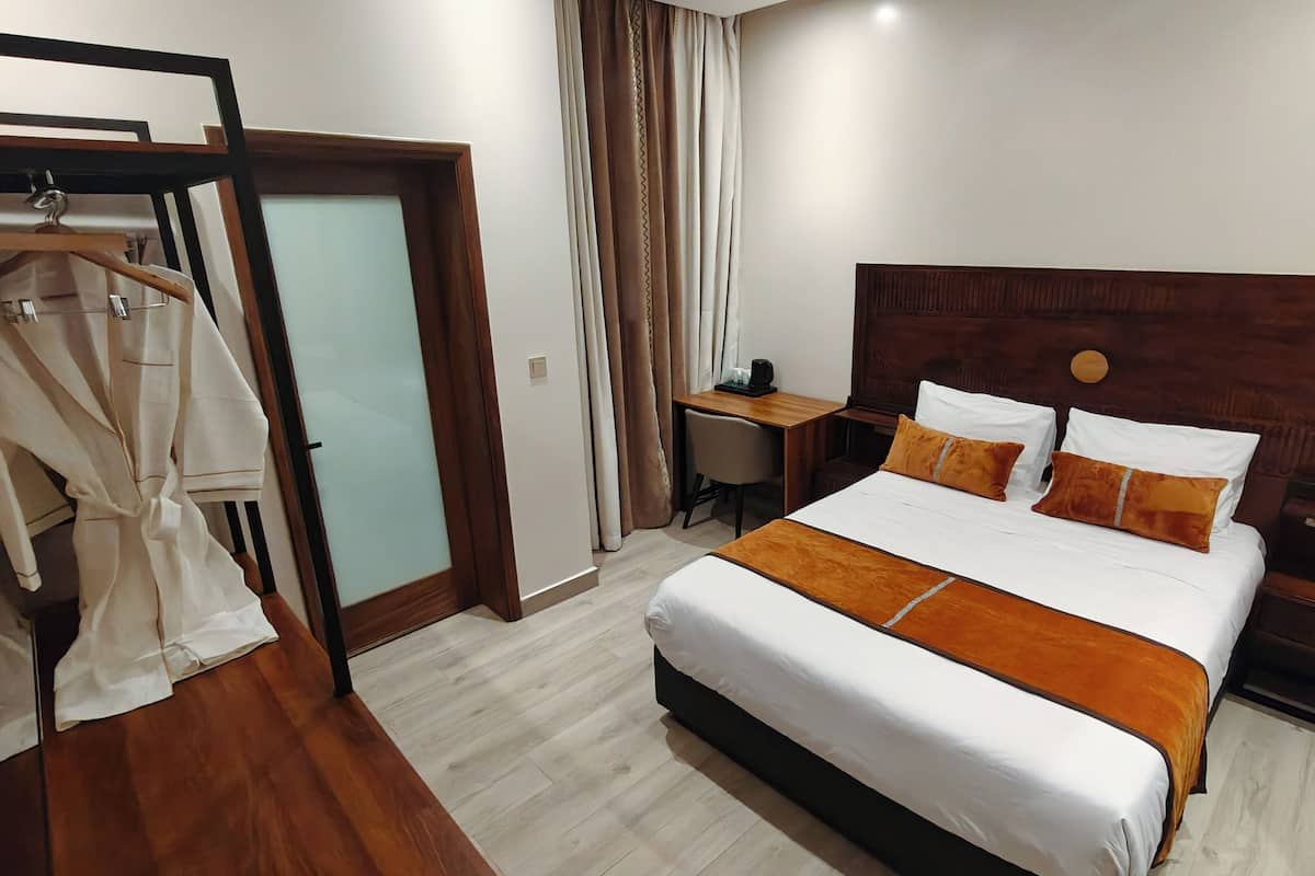 A hotel room with a bed, a desk, a chair, a wardrobe, and a window with curtains.