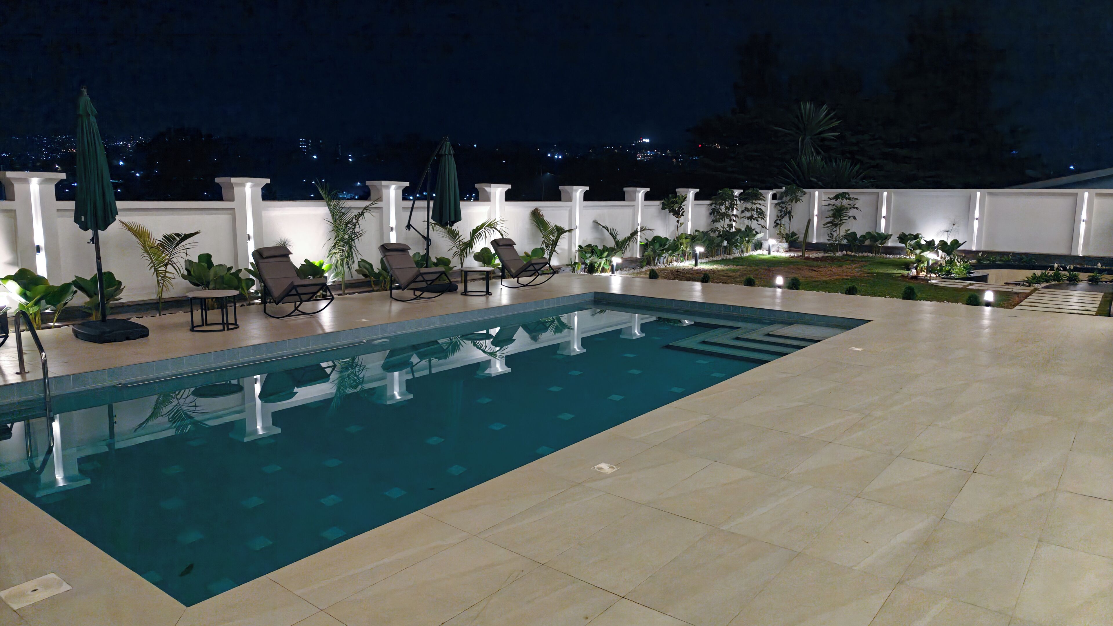An indoor swimming pool with lounge chairs and umbrellas, surrounded by potted plants and a white railing.