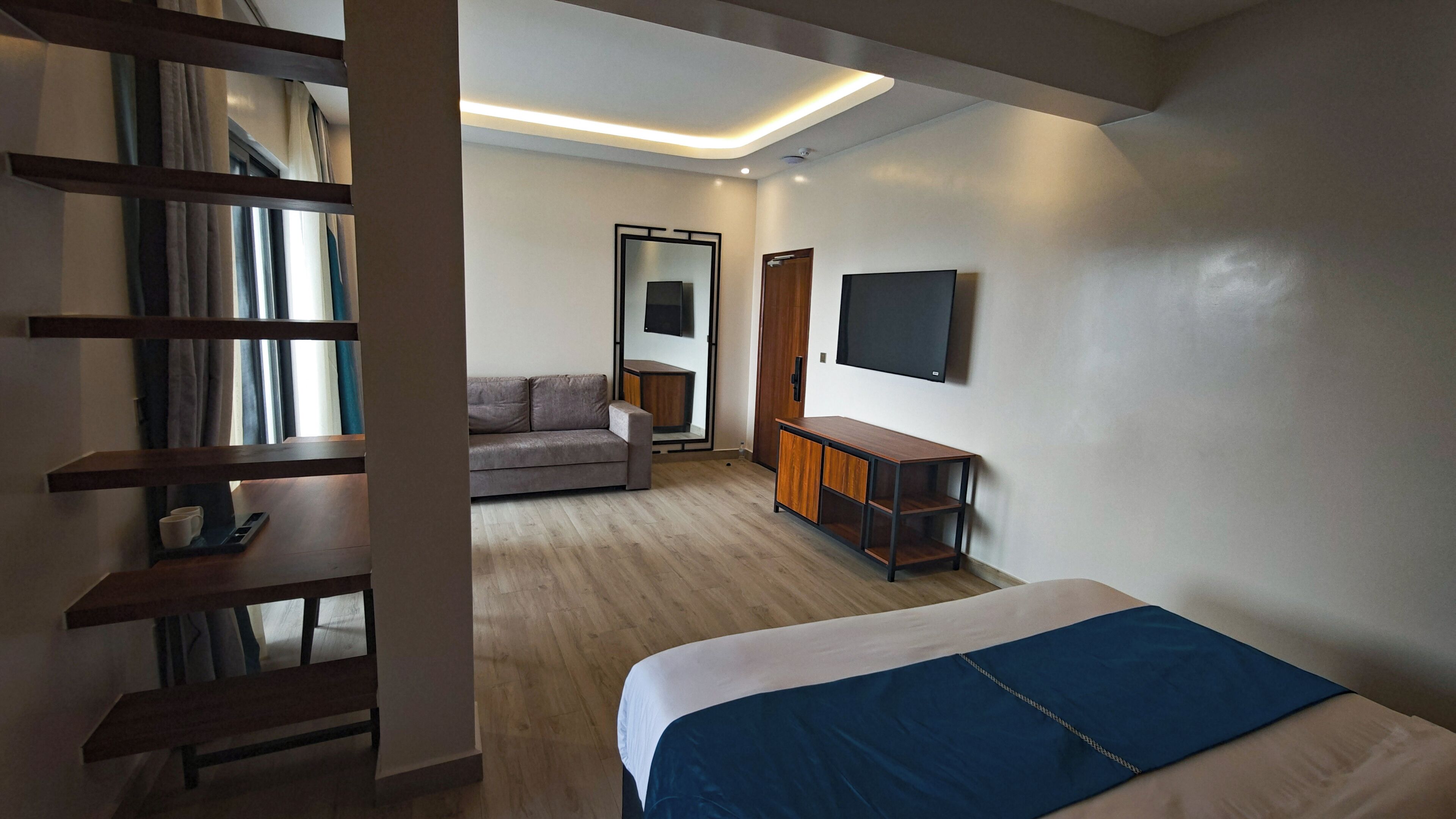 A modern hotel room with a bed, a sofa, a TV, and a wooden cabinet.