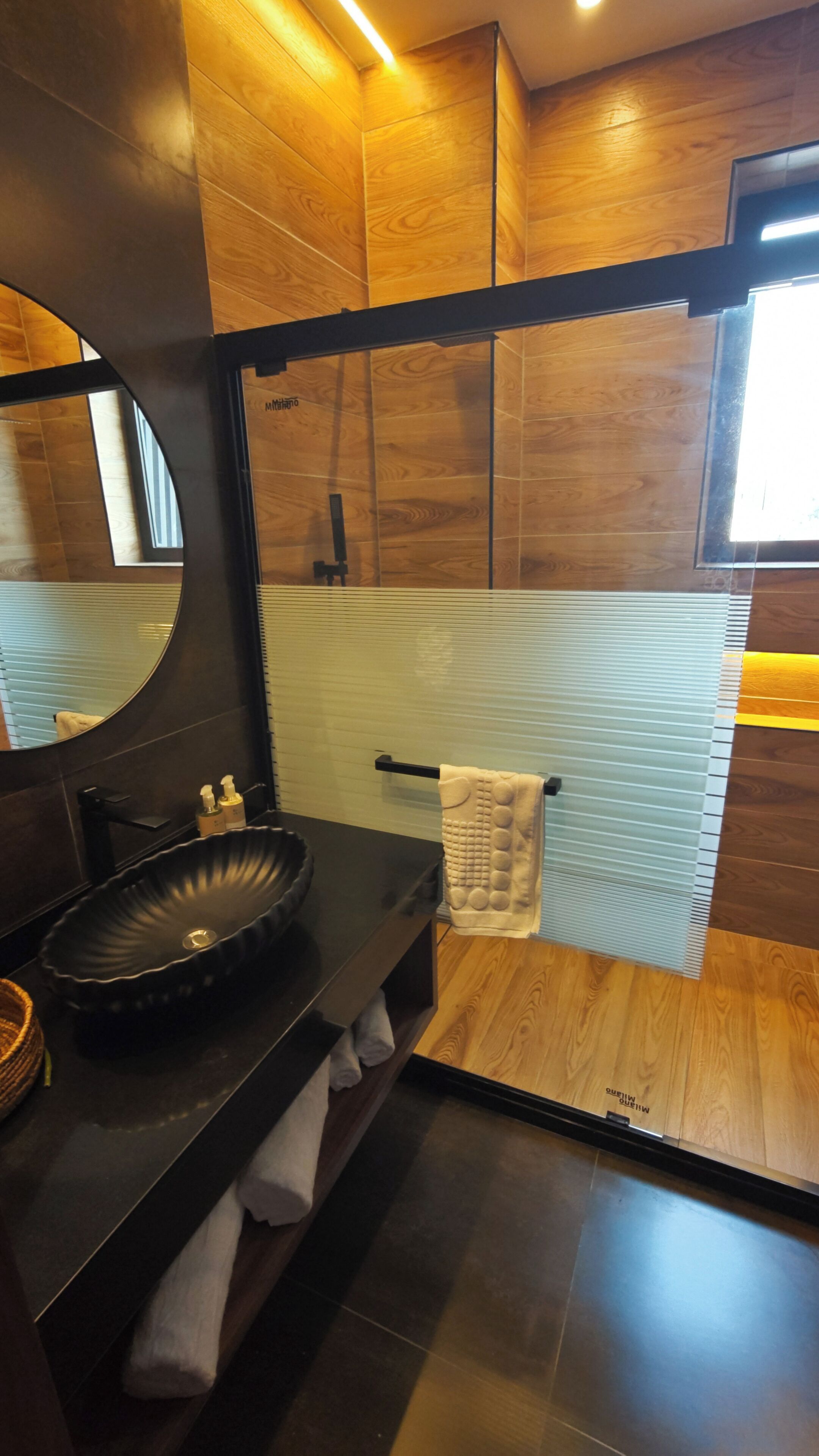 Un baño moderno con un lavabo negro, un espejo grande y un perchero para toallas.