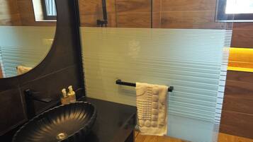 Un baño moderno con un lavabo negro, un espejo grande y un perchero para toallas.