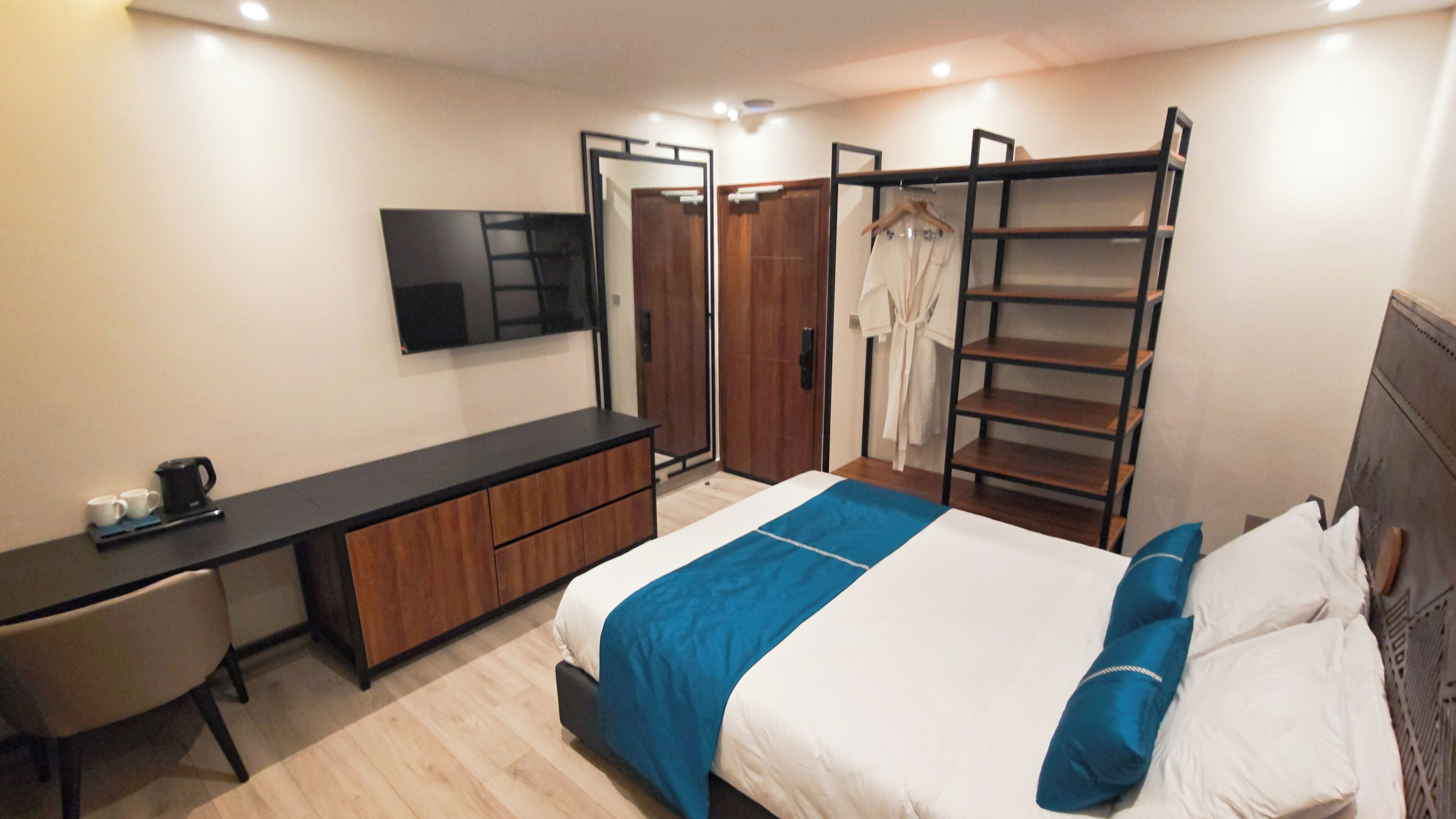 A modern hotel room with a bed, a desk, a TV, and a wardrobe.