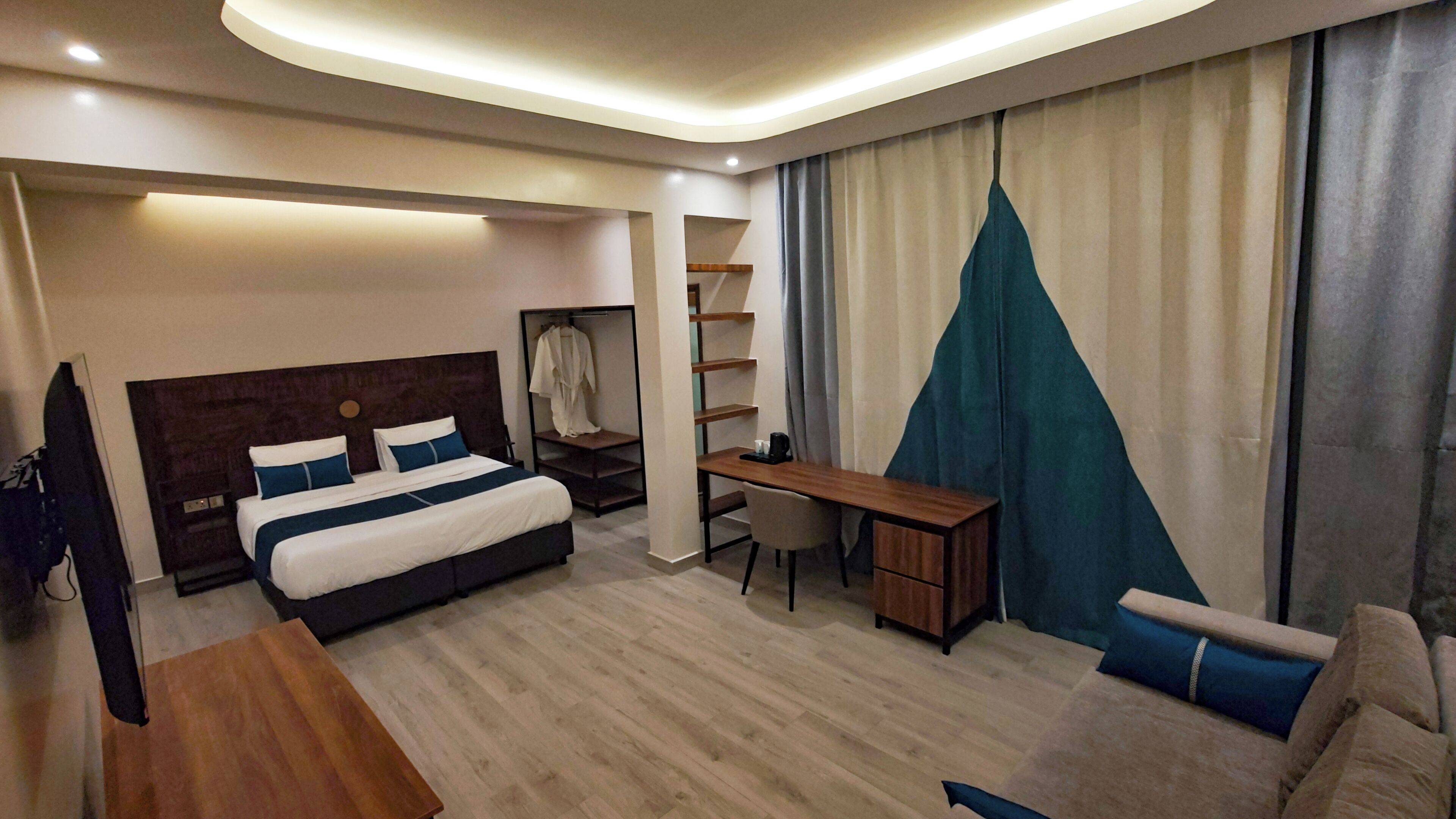 A modern hotel room with a large bed, a desk, a chair, and a TV.