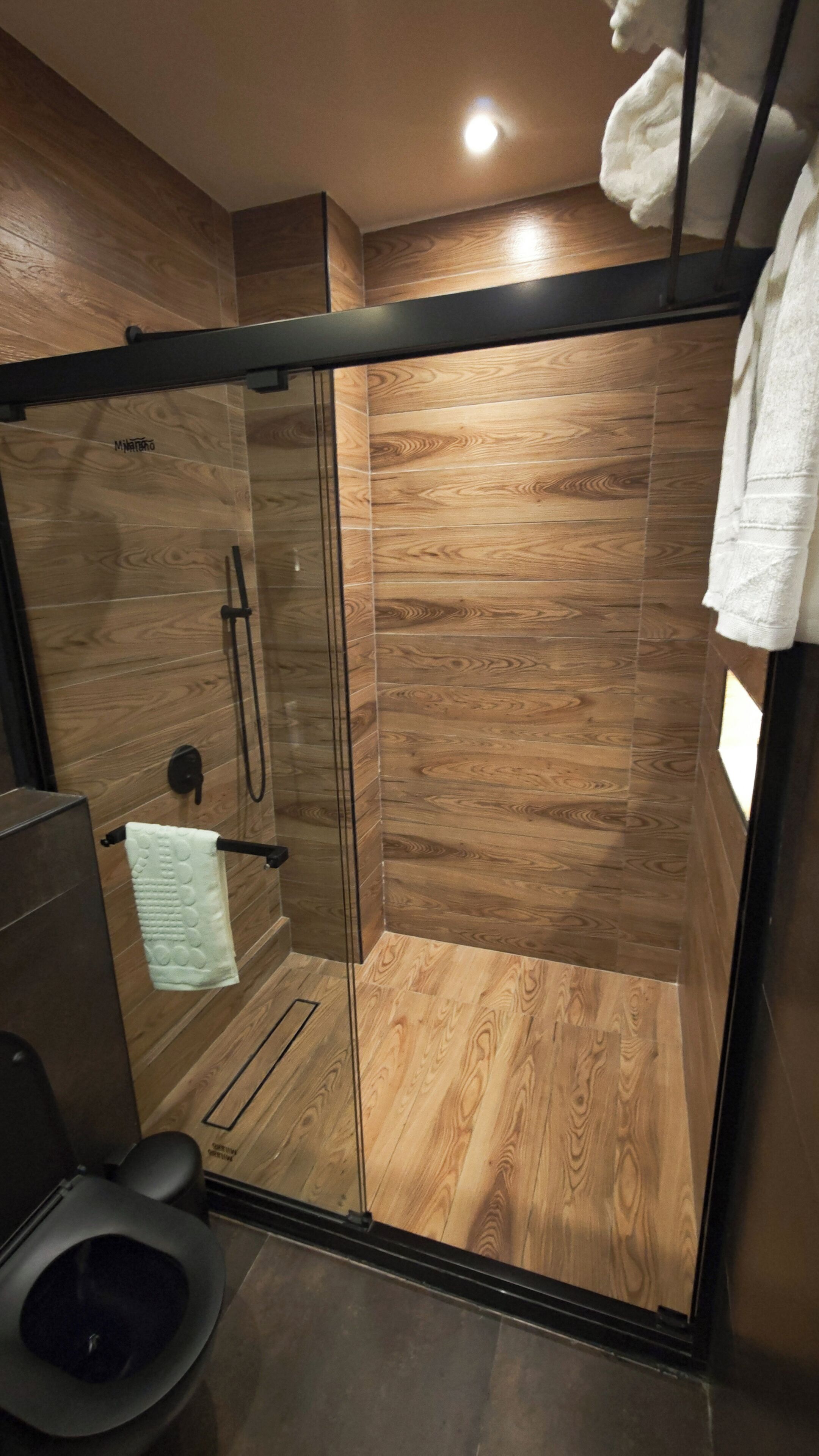 A modern shower stall with a glass door, wooden panel walls, and a black frame.