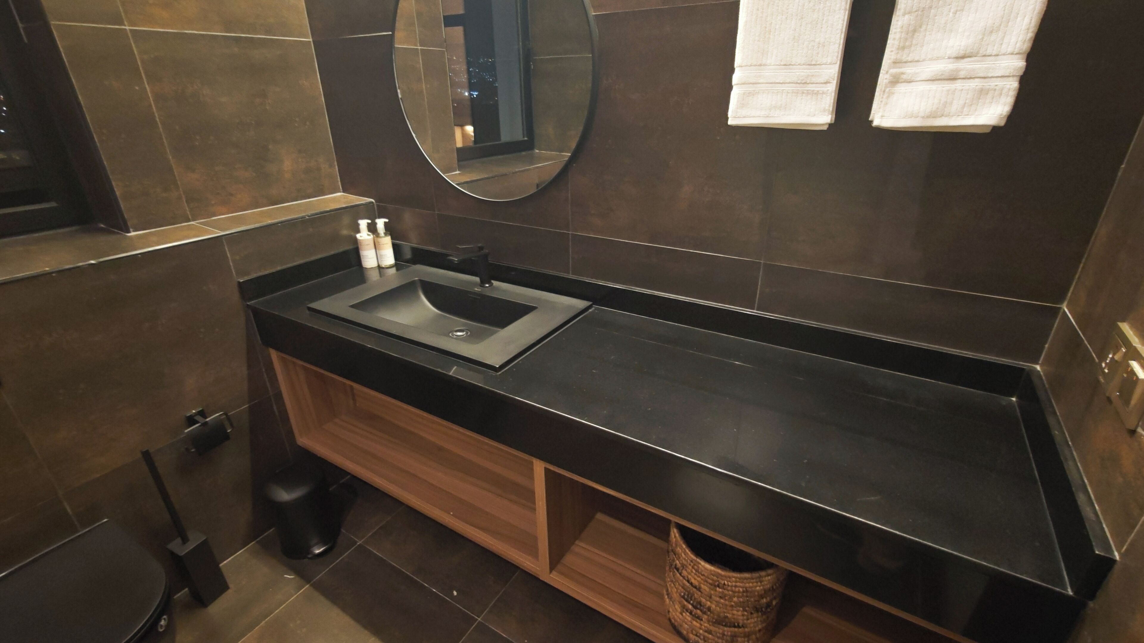 A modern bathroom with a black countertop, a sink, a mirror, and a wooden cabinet.