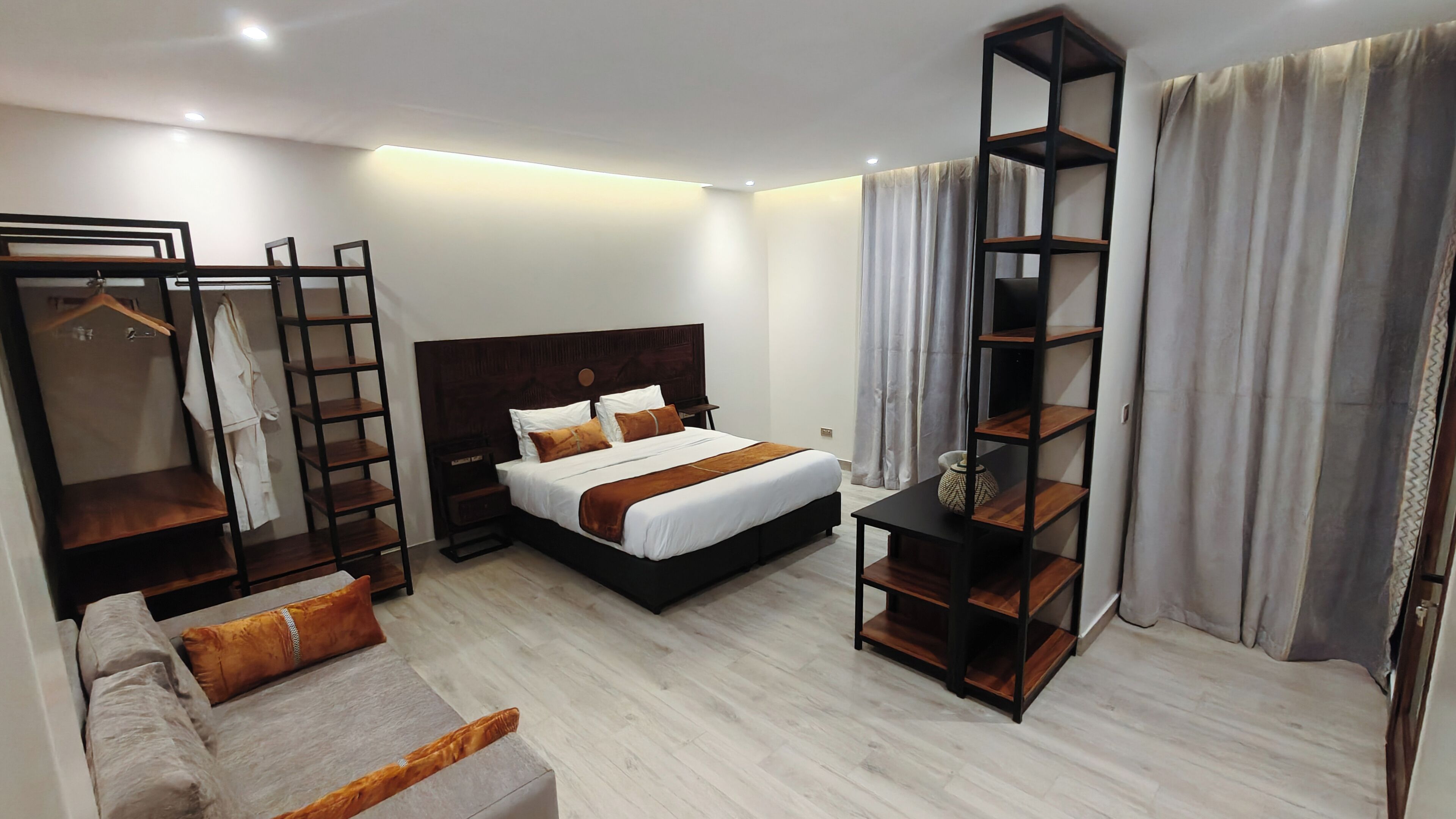 A modern hotel room with a bed, a wardrobe, a seating area, and a tall shelving unit.
