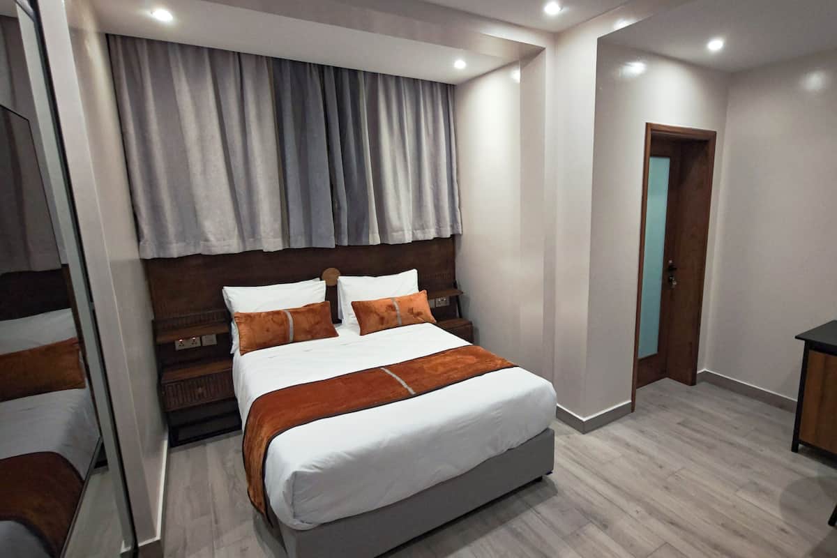 A modern bedroom with a large bed, a desk, and a door.