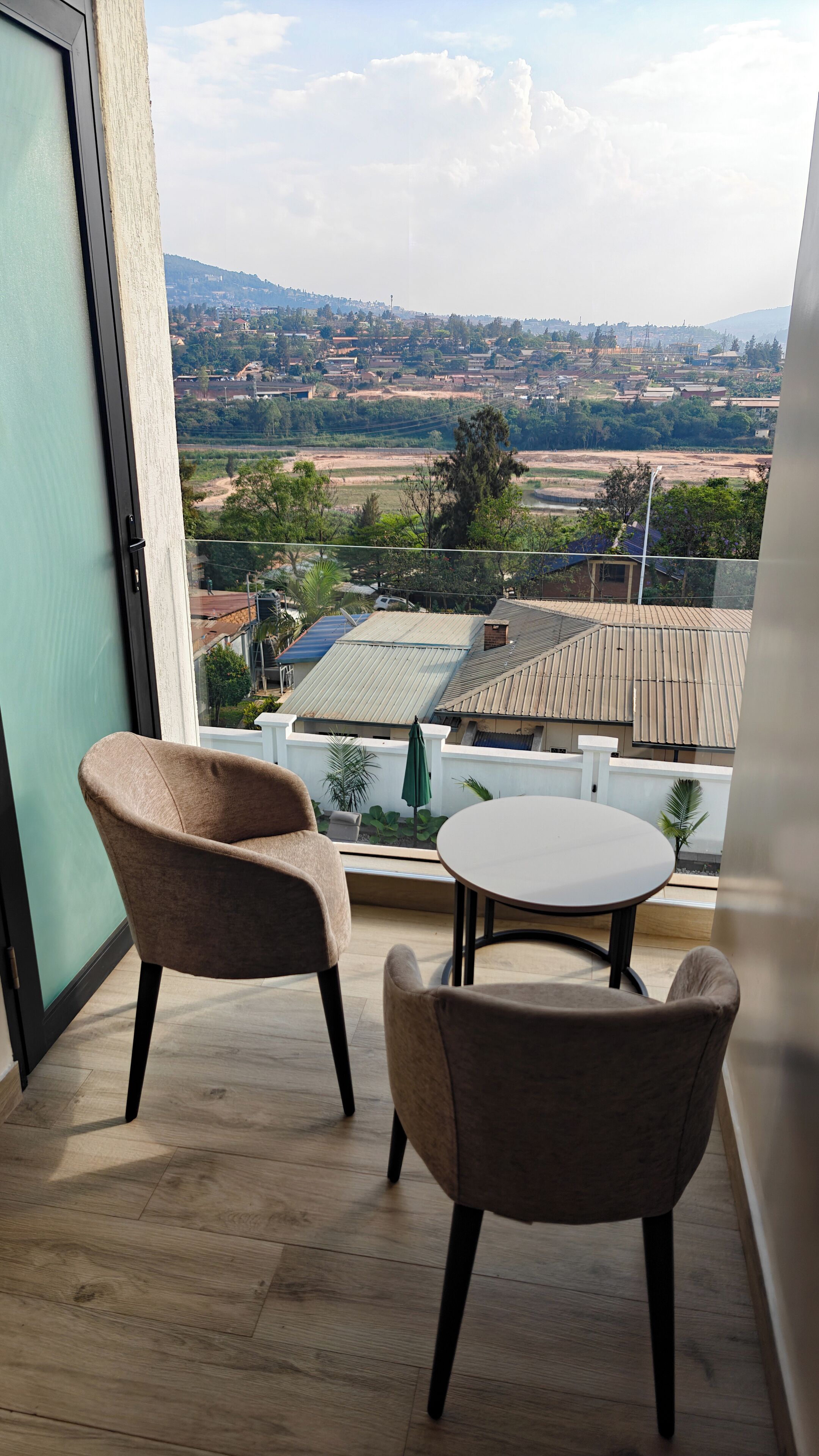 Un balcon avec deux chaises et une table, donnant sur un quartier résidentiel avec des maisons et de la verdure.