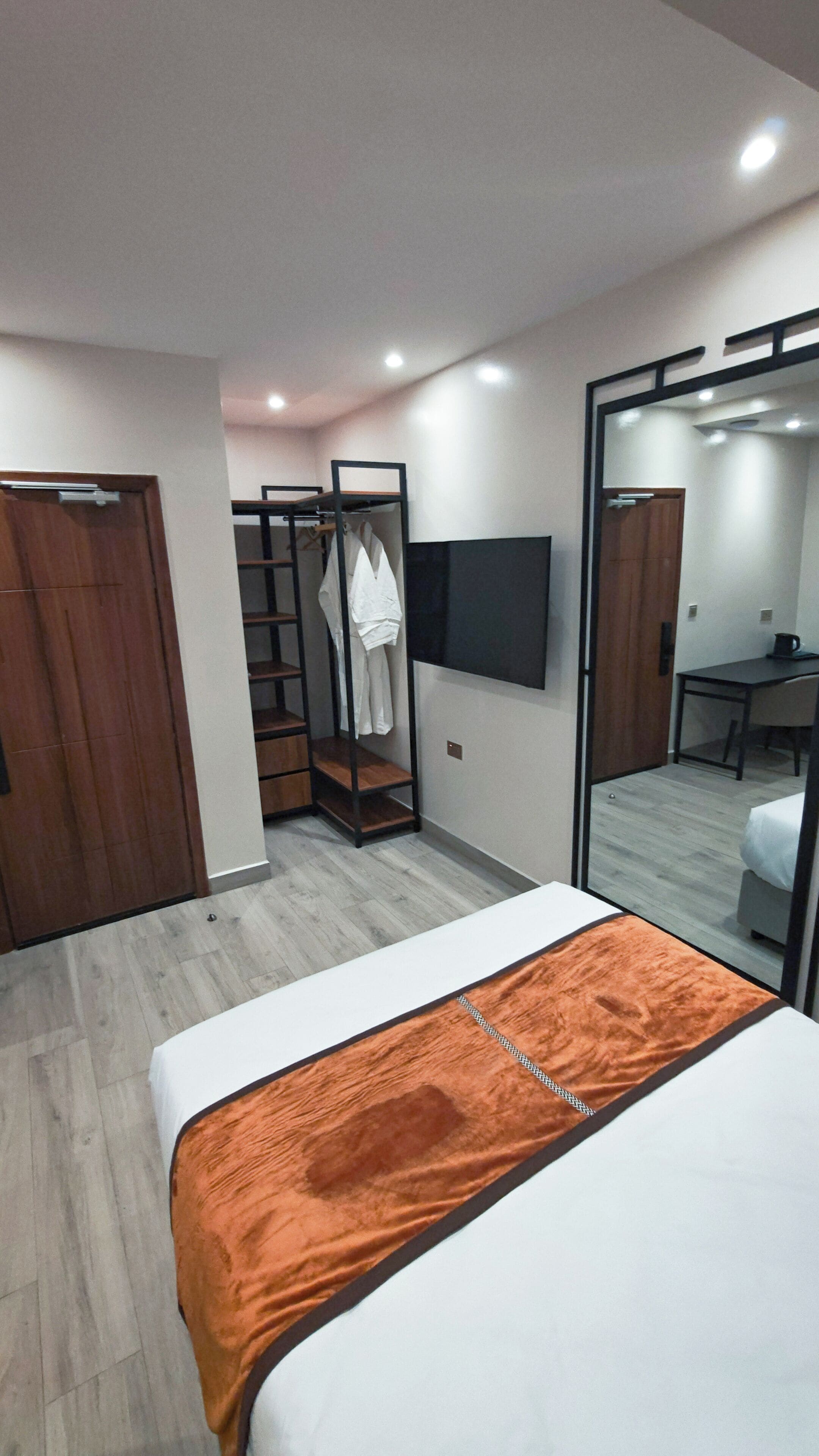 Une chambre d’hôtel moderne équipée d’un lit, d’une armoire, d’un téléviseur fixé au mur et d’un miroir.