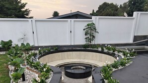 Un jardín ajardinado con un espacio de descanso curvo, rodeado por un muro blanco y diversas plantas.