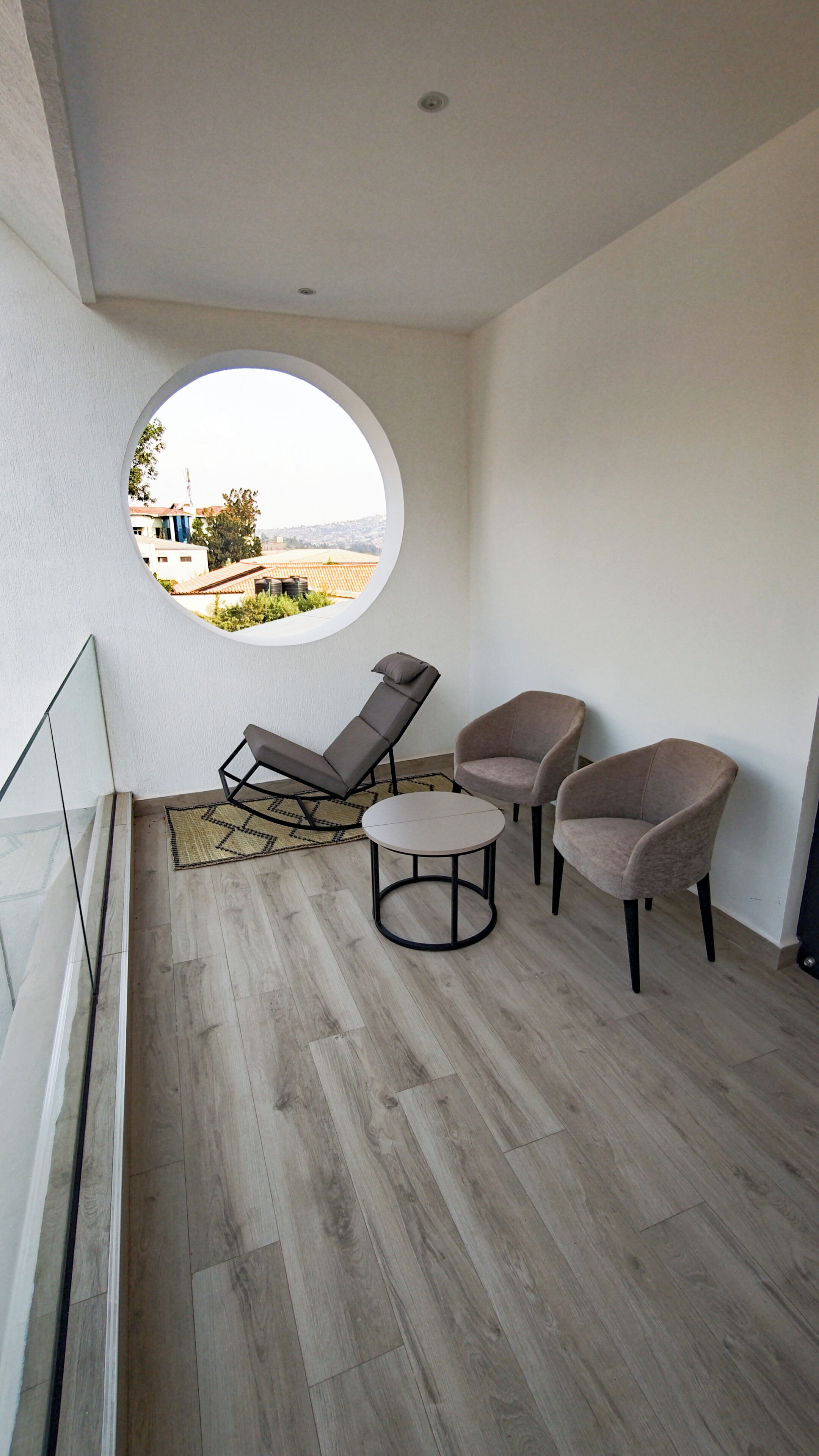 A modern balcony with a circular window, two lounge chairs, and a small table.