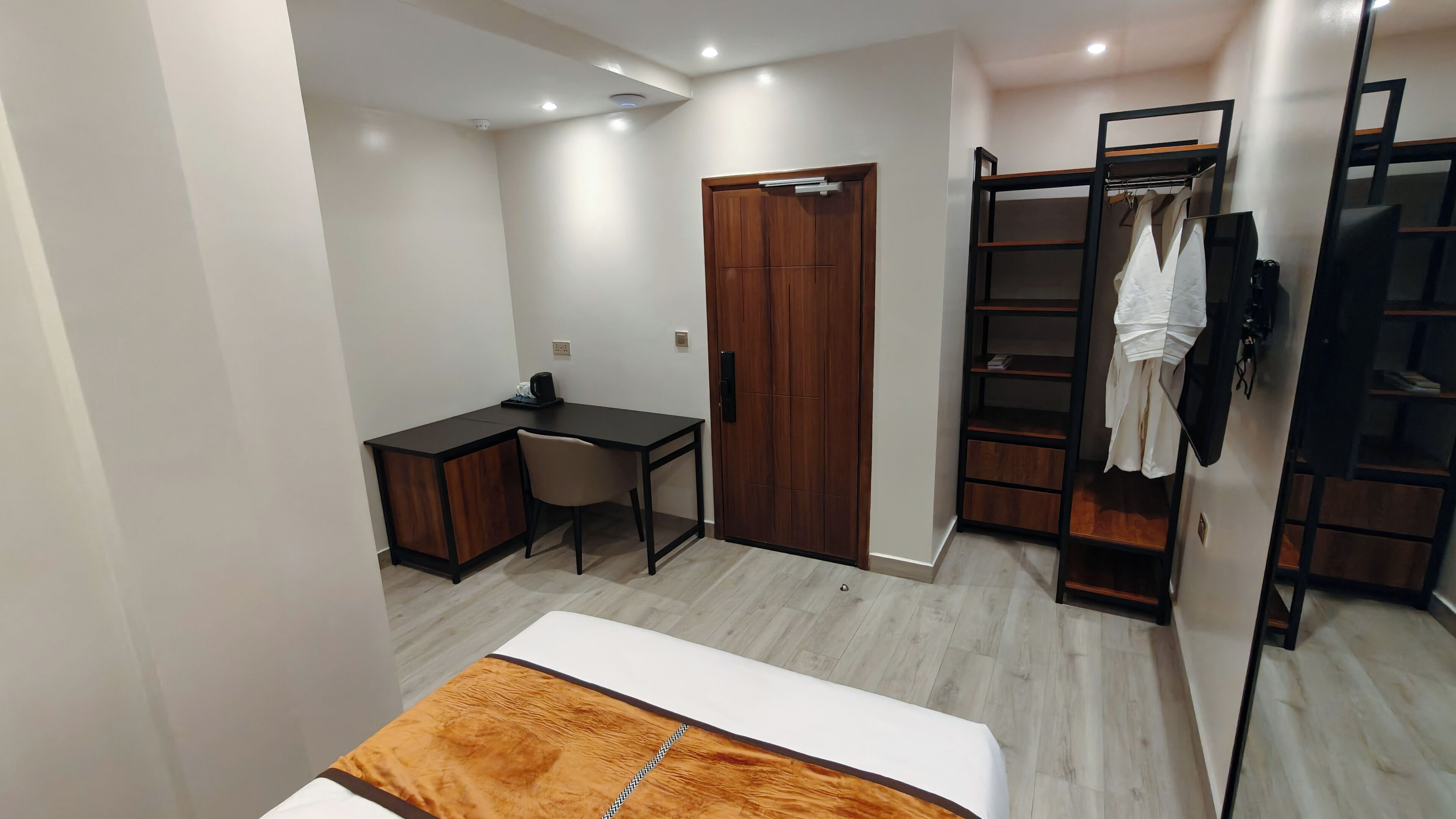 A bedroom with a bed, a desk, a chair, a wardrobe, and a shelving unit.