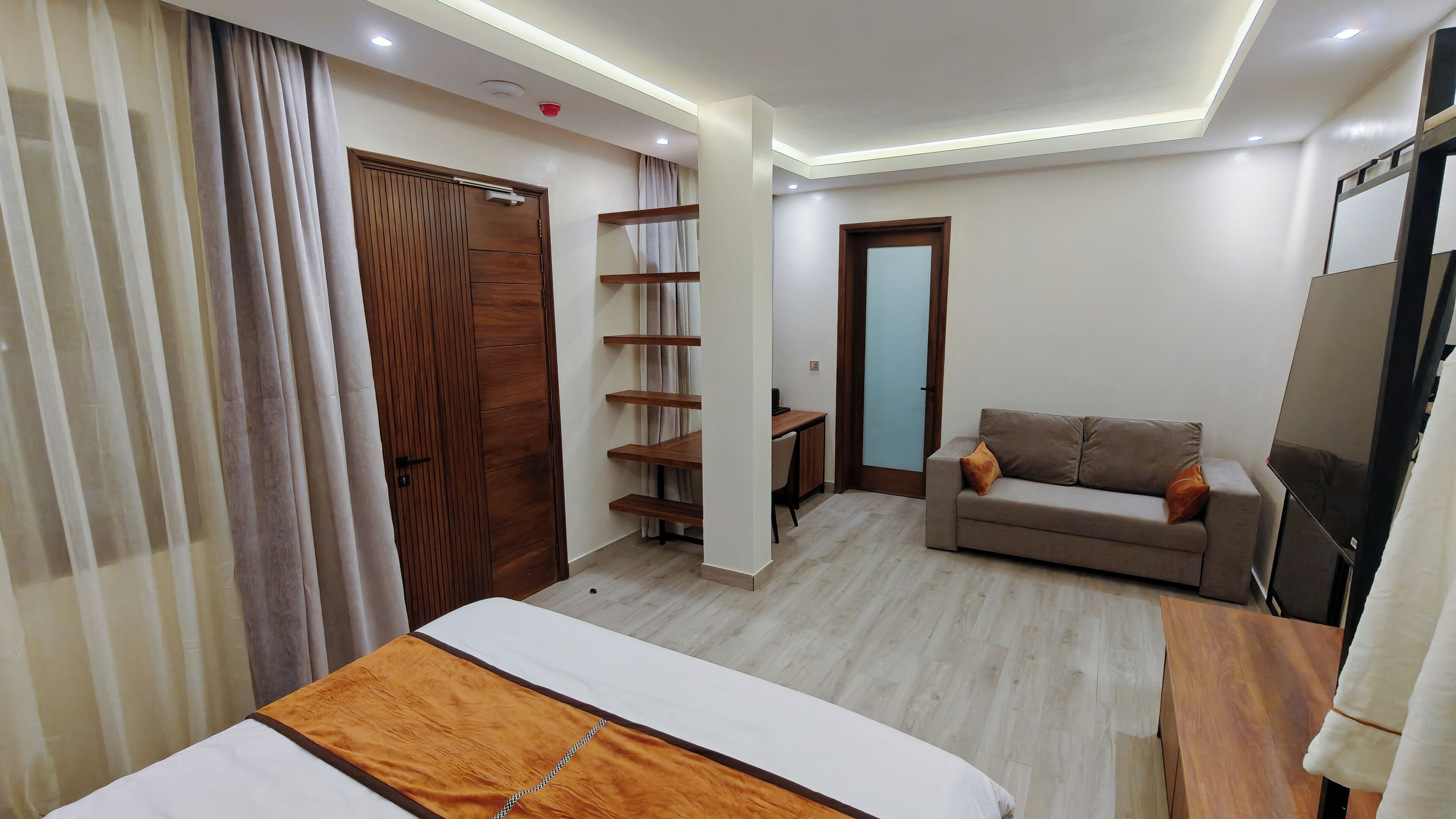 A modern hotel room with a bed, a sofa, a desk, and a TV.