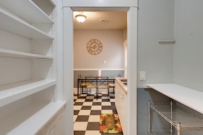 A kitchen with a checkered floor, a clock on the wall, and a welcome mat.
