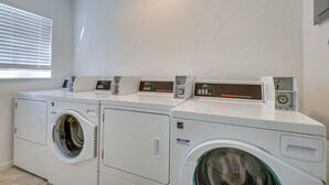 Un área de lavandería con tres lavadoras apiladas, un panel de control y una ventana con persianas.