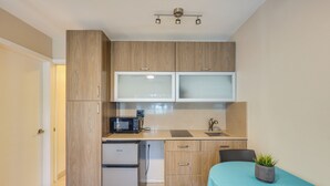 Una cocina compacta con armarios de madera, un microondas, un refrigerador y un lavamanos.