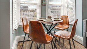 A dining area with a round table, four brown chairs, and a bay window with white blinds. - Walk to Beach & Boardwalk: Ocean City Haven! (Ocean City)