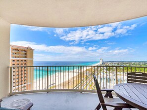 Un balcón con vista a una playa y un muelle, con un edificio alto al fondo.