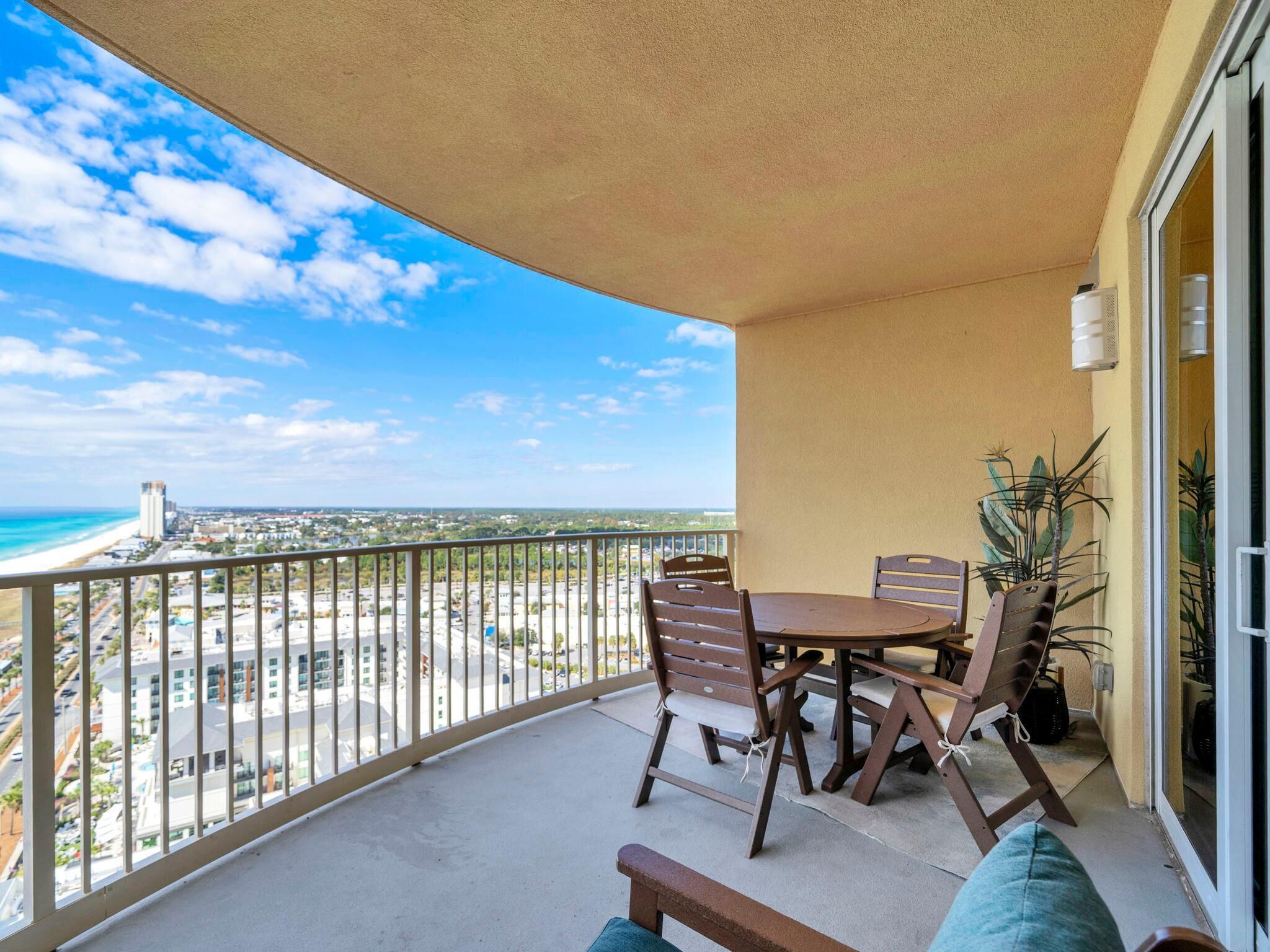 Ein Balkon mit Tisch und Stühlen, Blick auf den Strand und ein Gebäude in der Ferne.