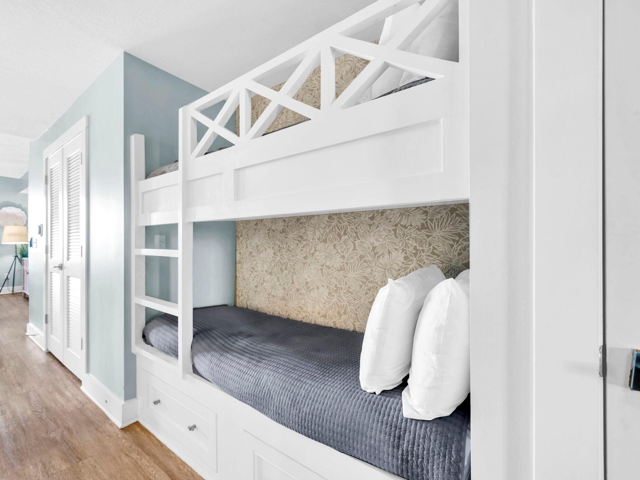 A bunk bed with a white frame, a grey mattress, and white pillows.