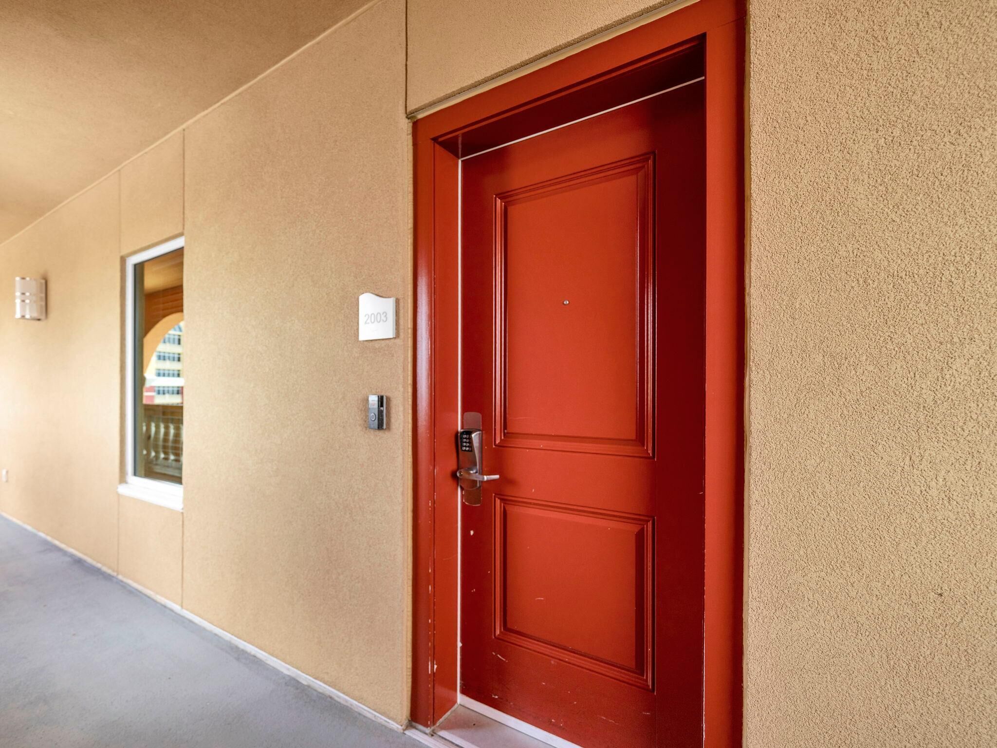 A red door with a keypad lock, a small sign with the number 2003, and a window to the left.