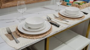 A dining table set with white plates, bowls, cutlery, and wine glasses, with a woven placemat and a wooden-framed mirror above. - Modern Studio w King Bed, Full Kitchen, Gated Yard (Spring Valley)