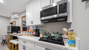A modern kitchen with white cabinets, a stainless steel microwave, and a gas stove. - Modern Studio w King Bed, Full Kitchen, Gated Yard (Spring Valley)