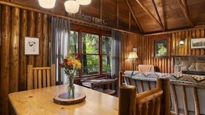 Interior de una cabaña de madera con una mesa de comedor, un sofá y una chimenea.