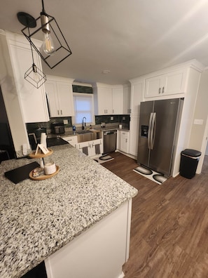 A kitchen with white cabinets, a stainless steel refrigerator, granite countertops, and a wooden island.