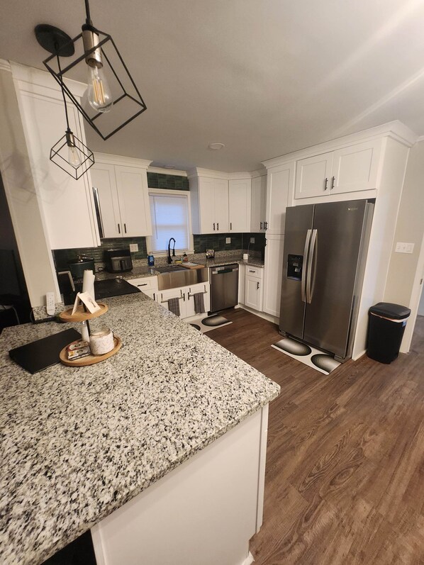 A kitchen with white cabinets, a stainless steel refrigerator, granite countertops, and a wooden island.