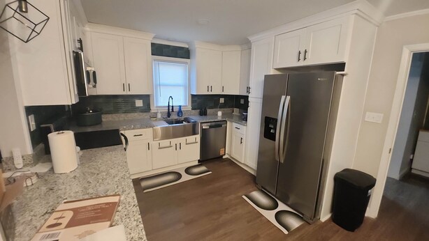 A modern kitchen with white cabinets, a stainless steel refrigerator, a granite countertop, and a built-in dishwasher.