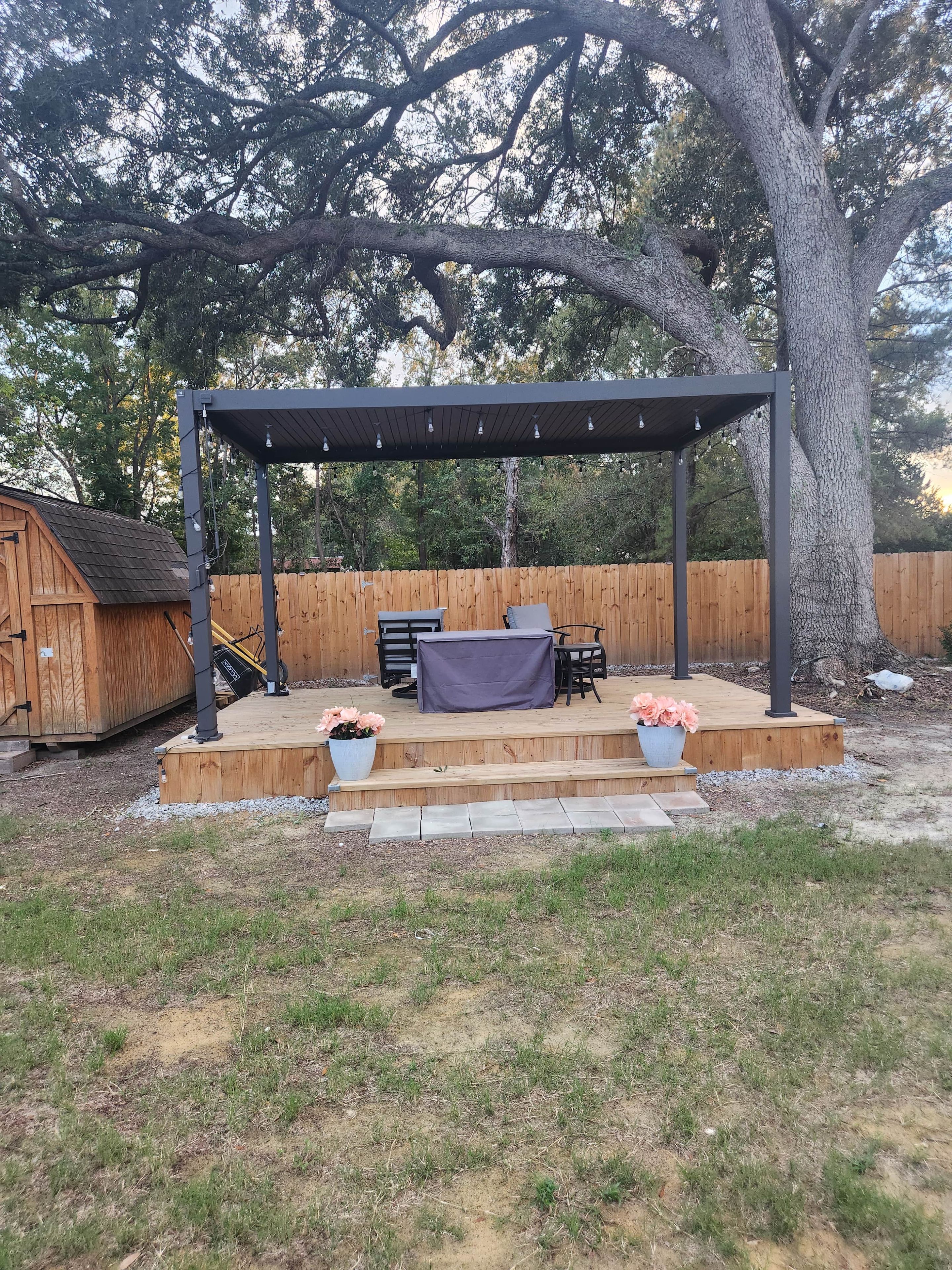 A wooden deck with a pergola, outdoor furniture, and potted plants.