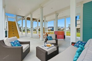 Un patio techado al aire libre con mobiliario de mimbre, una escalera de madera y vistas a casas en el fondo.