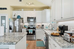 A modern kitchen with white cabinets, stainless steel appliances, and a granite countertop. - Sea Isle Beach Fenced Yard (Galveston)
