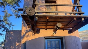 A rustic building with a blue door, a wooden porch, and a stone base. - Skier's Hideaway in Los Cerrillos (Los Cerrillos)
