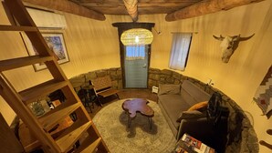 A cozy interior with a stone wall, wooden furniture, a round rug, and a ceiling fan. - Skier's Hideaway in Los Cerrillos (Los Cerrillos)