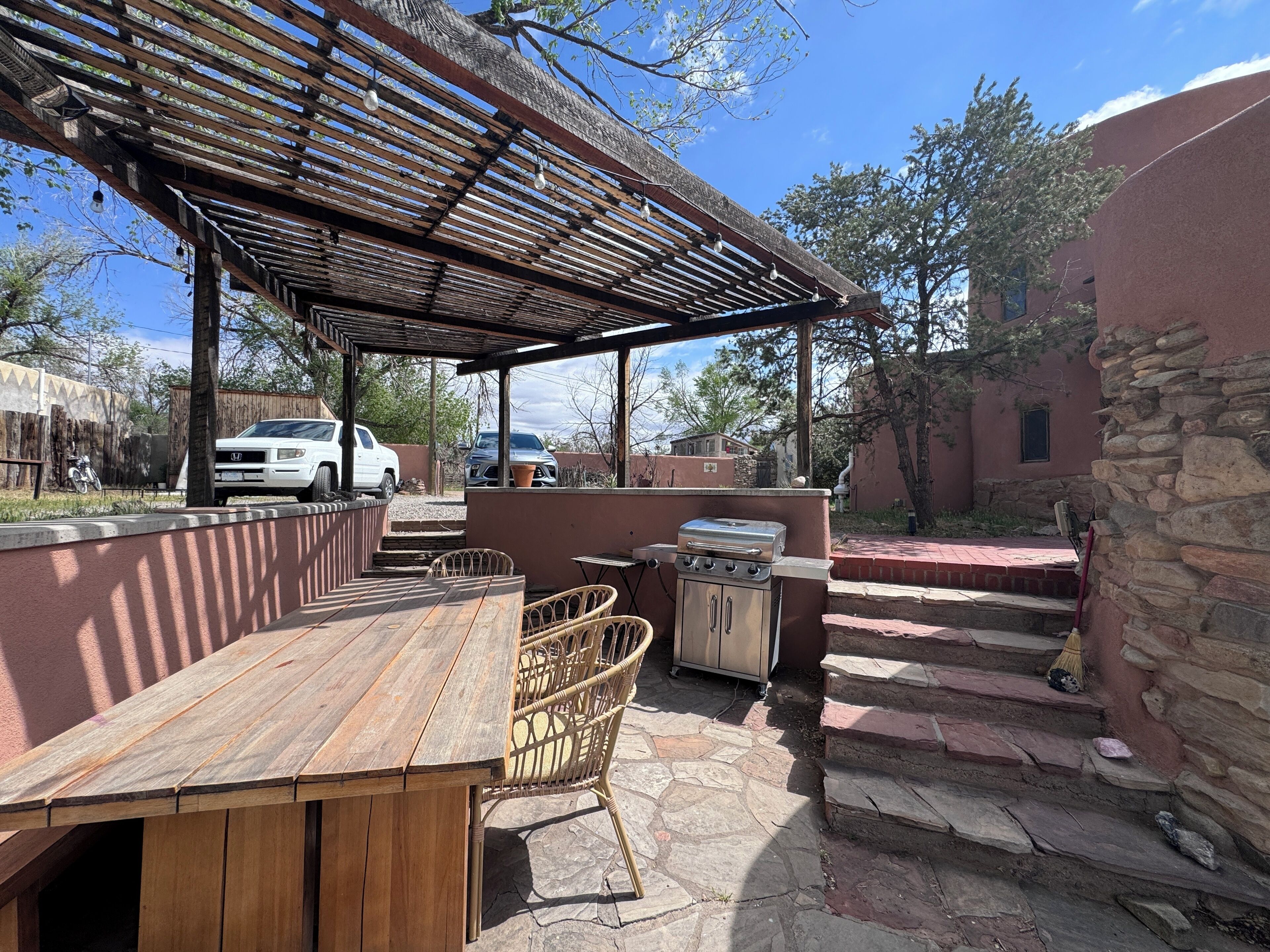 Une terrasse extérieure avec une table et des chaises en bois, un barbecue et un espace salon abrité.